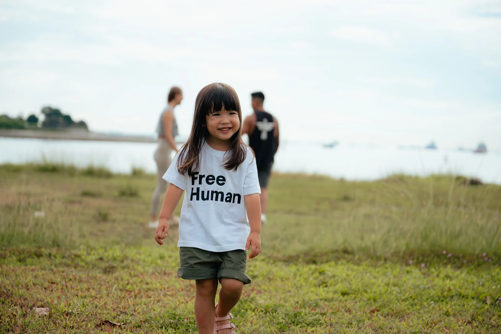 A family moment by the water, with a child in a Free Human T-shirt in the foreground